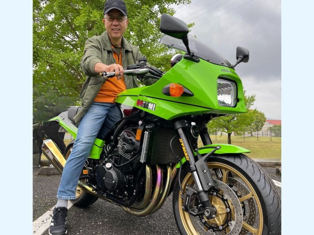還暦ライダーの筆者が展示会でまたがる緑色の大型バイク。所有への憧れを抱く様子。