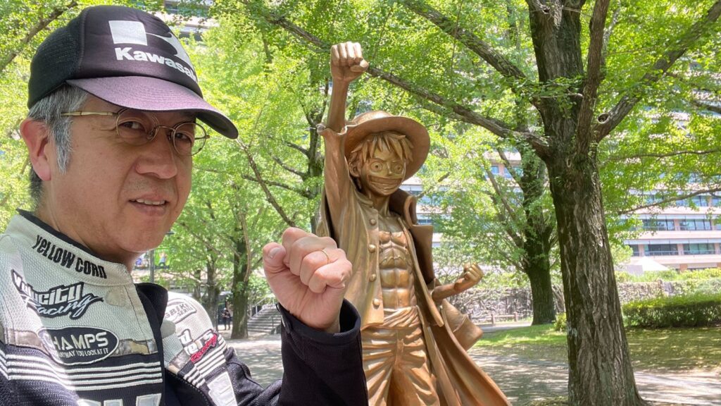 熊本のルフィ像と同じポーズで拳を突き上げる、バイク歴40年超の筆者。