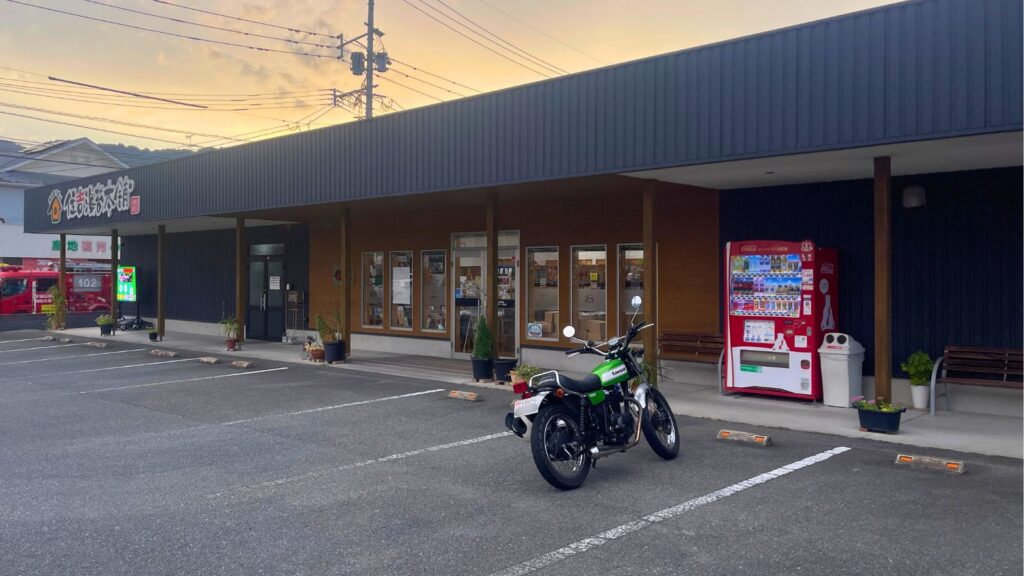 熊本・住吉海苔本舗の店舗入口に停車したカワサキ250TR。隣にベンチと自動販売機があり、バイクツーリング後のライダーが一息つける休憩スペースとして最適。