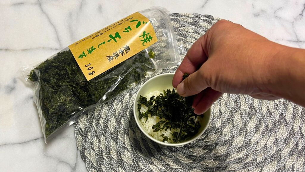 炊きたてご飯に住吉海苔本舗の焼バラ干し海苔をふりかける様子。社長直伝の食べ方であり、海苔の力強い磯の香りと旨味が口いっぱいに広がる瞬間を表現。
